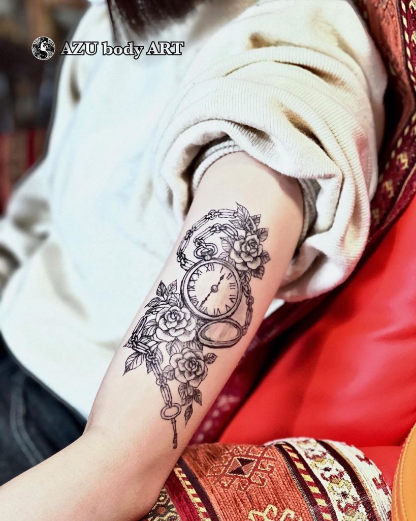 腕に女性向けの懐中時計と薔薇のタトゥー