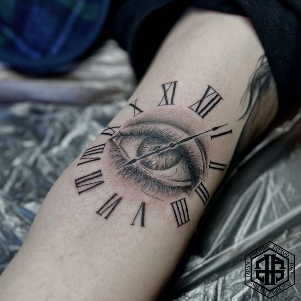 腕に目とローマ数字の時計のタトゥー