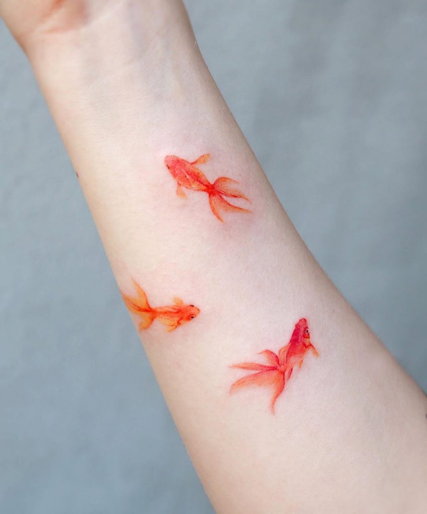 A cute small one-point tattoo of three watercolor goldfish on the wrist